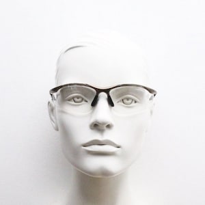 May include: A white mannequin head wearing a pair of brown and clear safety glasses.