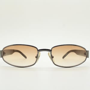 90s vintage oval sunglasses small bug eye with light tone lenses. Satin finish brown metal frame with black arms. 2000&#39;s. NOS