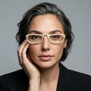 Puede incluir: Gafas con una montura de color crema con efecto mármol y un diseño de puente distintivo. Las lentes son transparentes y presentan el texto GanniVertical impreso en la lente derecha. La montura tiene forma rectangular con bordes redondeados.