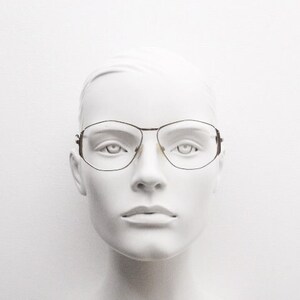 Puede incluir: Una cabeza de maniqu&iacute; blanca que lleva unas gafas finas con montura met&aacute;lica de forma rectangular.