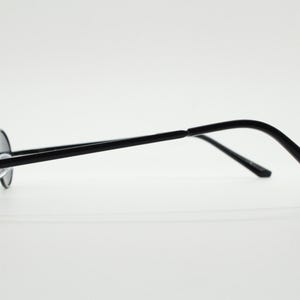 May include: Black round sunglasses with a thin, black metal frame. The lenses are dark, and the temples curve gently for a comfortable fit. The glasses are designed in a classic style.
