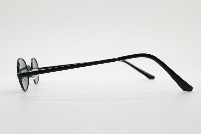 May include: Black round sunglasses with a thin, black metal frame. The lenses are dark, and the temples curve gently for a comfortable fit. The glasses are designed in a classic style.
