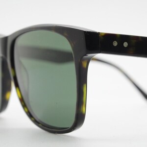 Puede incluir: Gafas de sol de carey negro y marr&oacute;n con lentes verdes. Las gafas tienen una forma rectangular cl&aacute;sica y un fino marco de metal.