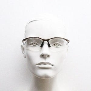 May include: Clear-lens eyeglasses with a dark brown frame. The glasses are displayed on a white mannequin head. The frames have a sleek, modern design, and the lenses are clear, offering a full view.