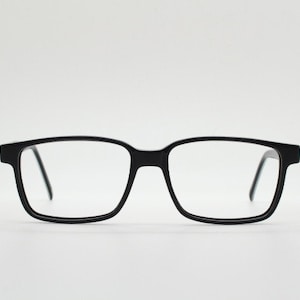 Könnte beinhalten: Schwarze rechteckige Brille mit schlichtem Design.