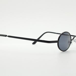 May include: Black round sunglasses with dark gray lenses. The glasses have a thin, black metal frame and straight temples. The lenses are circular and the nose bridge is a silver metal.