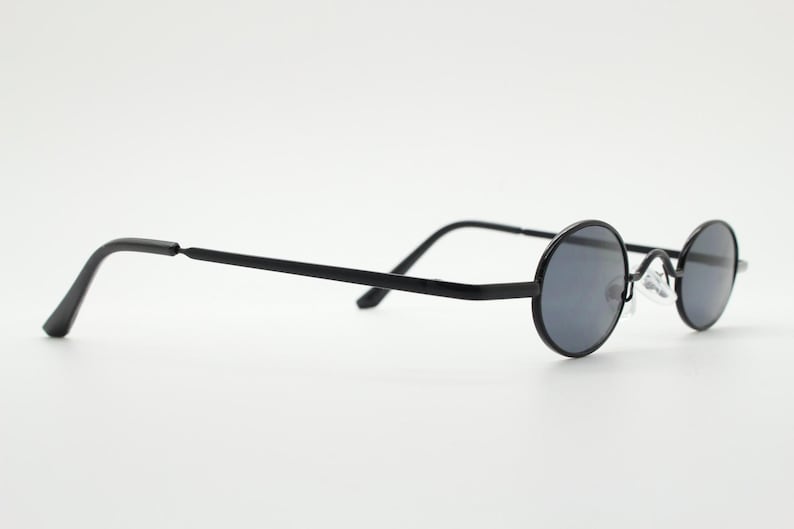 May include: Black round sunglasses with dark gray lenses. The glasses have a thin, black metal frame and straight temples. The lenses are circular and the nose bridge is a silver metal.