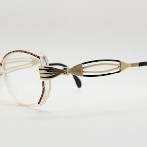 May include: Clear plastic framed glasses with a brown and gold trim. The arms are black with a gold wire design.