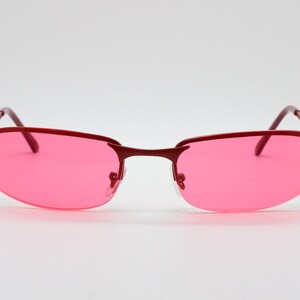 May include: Red sunglasses with pink lenses. The sunglasses have a rimless design and a thin metal frame.