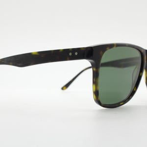 Puede incluir: Gafas de sol de carey con lentes verdes. Las gafas tienen una forma rectangular cl&aacute;sica y un marco delgado.