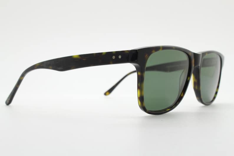 Puede incluir: Gafas de sol de carey con lentes verdes. Las gafas tienen una forma rectangular cl&aacute;sica y un marco delgado.