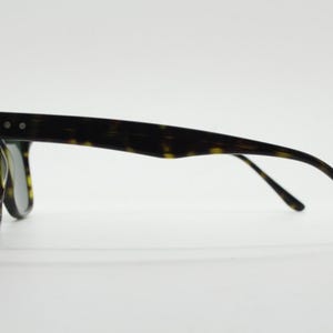 Puede incluir: Gafas de sol con montura de carey y lentes oscuras. Las gafas tienen un estilo cl&aacute;sico y retro.