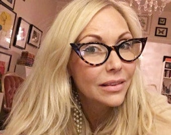 May include: Cat-eye glasses with a brown and black tortoiseshell pattern frame. The eyewear features a pointed outer edge design and clear lenses, providing a distinct look that frames the face with a classic, sharp, and angular aesthetic.