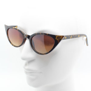 May include: Tortoise shell cat eye sunglasses with brown gradient lenses. The sunglasses are on a white mannequin head.