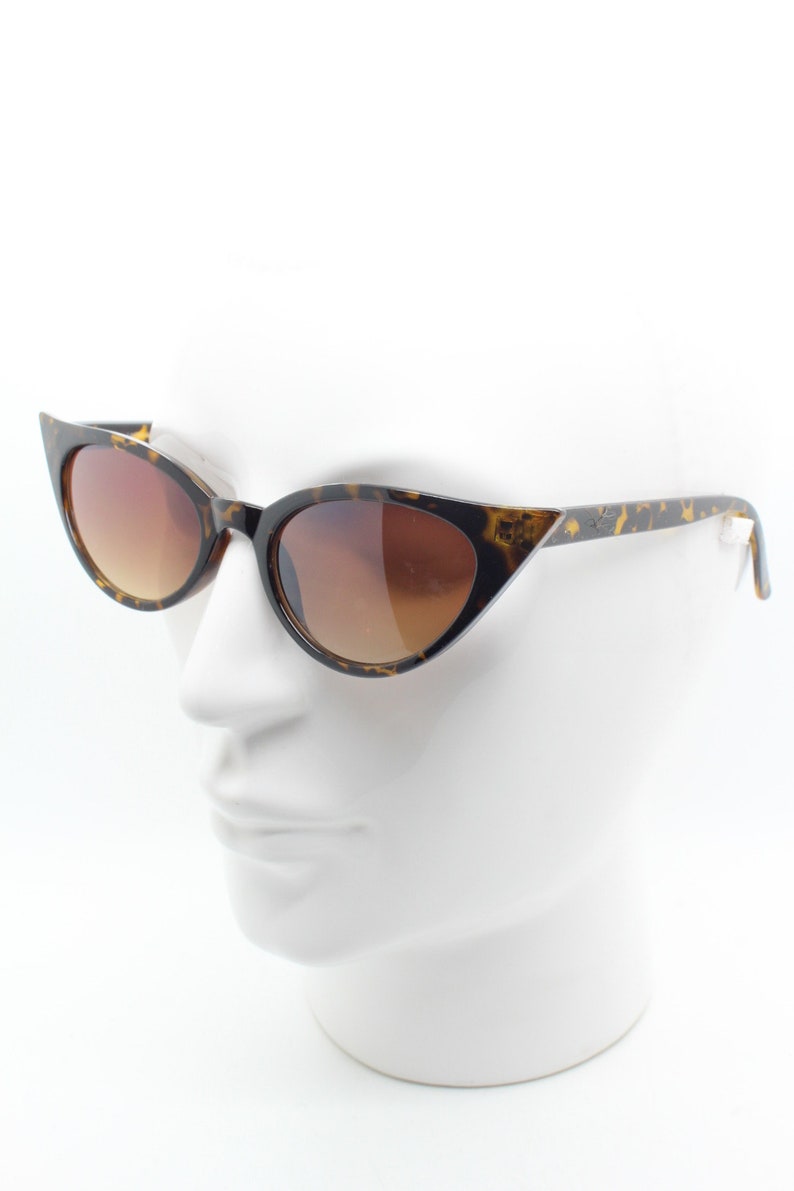 May include: Tortoise shell cat eye sunglasses with brown gradient lenses. The sunglasses are on a white mannequin head.