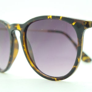 Lunettes de soleil vintage des années 90. Monture brillante en tortue avec lentilles noires graduées et bras dorés contrastants. NOS inutilisés