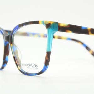 May include: Full-rim spectacles featuring a tortoiseshell pattern in shades of brown, black, and bright blue. The frames have a rectangular shape with rounded edges. The text BROOKLYN BLACK LABEL is printed on the right lens of the glasses.