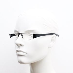 May include: A black, rimless, rectangular-shaped eyeglasses frame with clear lenses. The frame has a thin, metal design and is worn by a white mannequin.