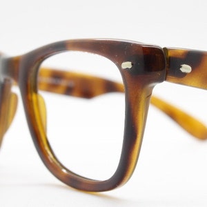 Può includere: Occhiali da vista in tartaruga con montatura marrone e lenti trasparenti. Gli occhiali hanno uno stile classico e retrò.