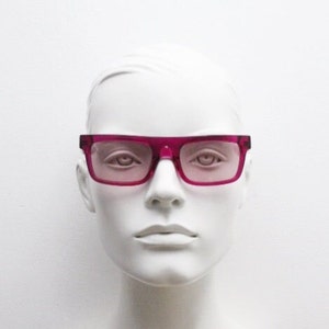 Könnte beinhalten: Eine Mannequin, die eine Brille mit rosafarbenem Kunststoffgestell und rosafarbenen Gläsern trägt.
