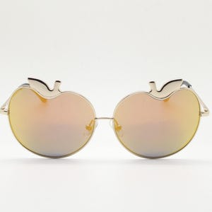 May include: Stylish sunglasses with a gold frame and gradient lenses. The frames are apple-shaped, with a stem detail at the top. The lenses have a mirrored finish, reflecting a range of colours.