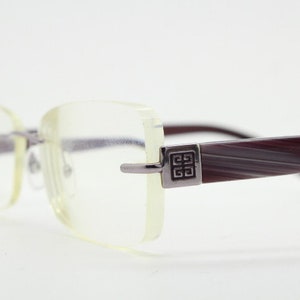 May include: A pair of clear, rectangular eyeglasses with a burgundy and white striped frame. The frame has a silver metal accent with a square logo.