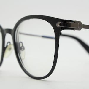 May include: Black eyeglasses with a metal frame and clear lenses. The brand name "DKNY" is printed on the side of the frame.