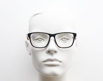 May include: A black framed pair of eyeglasses with clear lenses on a white mannequin head.