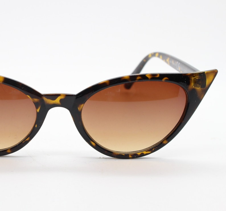 May include: Tortoise shell cat eye sunglasses with brown gradient lenses.
