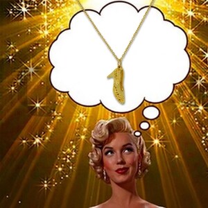 May include: A gold-toned necklace featuring a delicate chain and a pendant shaped like a high-heeled shoe. The pendant is suspended within a white thought bubble graphic that is positioned above a portrait of a person with blonde hair.