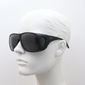 May include: Black sunglasses with a wraparound design, featuring dark lenses and a thick frame. The sunglasses are displayed on a white mannequin head, showcasing their shape and style. The text "POLAR SHIELD" is visible on the temple.