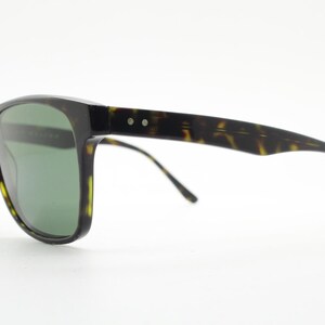 Puede incluir: Gafas de sol de carey con lentes verdes. Las gafas tienen una forma rectangular cl&aacute;sica y un fino marco de metal.