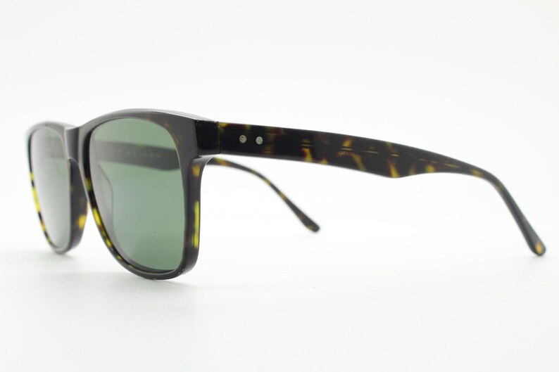 Puede incluir: Gafas de sol de carey con lentes verdes. Las gafas tienen una forma rectangular cl&aacute;sica y un fino marco de metal.