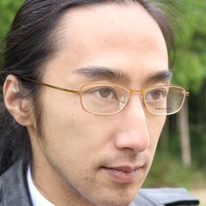 Puede incluir: Un hombre con el pelo largo y oscuro que lleva gafas de montura dorada. Está mirando a la derecha de la cámara.