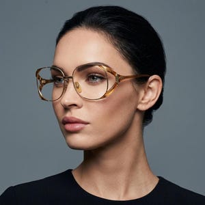 May include: Eyeglasses featuring a thin, gold-toned metal frame with an open-work design at the outer edges. The lenses are clear and oval-shaped, held by a delicate bridge and slender temples that extend toward the ears, creating a lightweight look.