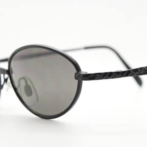 Occhiali da sole ovali vintage anni &#39;90. Montatura minimal in metallo nero opaco con insoliti motivi a dente di sega sulle aste. Mai usati e nuovi.