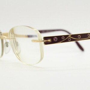 May include: Gold-rimmed glasses with clear lenses and a burgundy frame with small pink rhinestones.