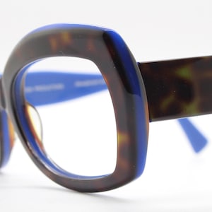 Könnte beinhalten: Blaue und Schildpatt-Brille mit abgerundetem, leicht eckigem Rahmen.