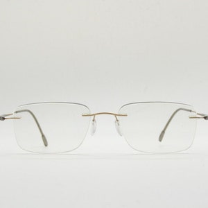 May include: A pair of rimless eyeglasses with a gold bridge and silver arms.