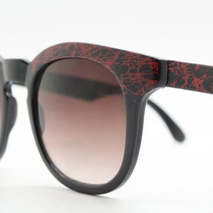80s vintage rounded wayfarer design sunglasses. Abstract patterned red brow and arms on a black frame with graduating  lenses. Unused NOS