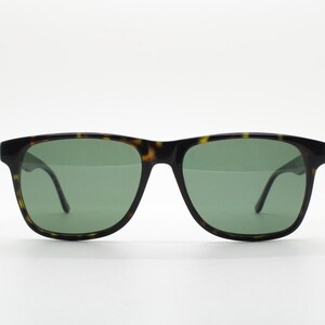 Puede incluir: Gafas de sol de carey con lentes verdes. Las gafas tienen una forma rectangular cl&aacute;sica.