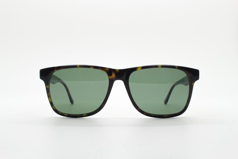Puede incluir: Gafas de sol de carey con lentes verdes. Las gafas tienen una forma rectangular cl&aacute;sica.