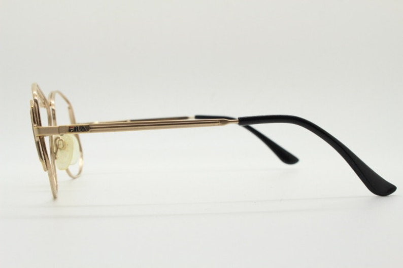 Puede incluir: Gafas de metal doradas con patillas de pl&aacute;stico negro. El nombre de la marca "FAUX" est&aacute; impreso en la montura.