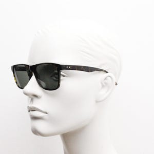 Puede incluir: Un par de gafas de sol de carey con lentes verde oscuro. Las gafas est&aacute;n en una cabeza de maniqu&iacute; blanca.