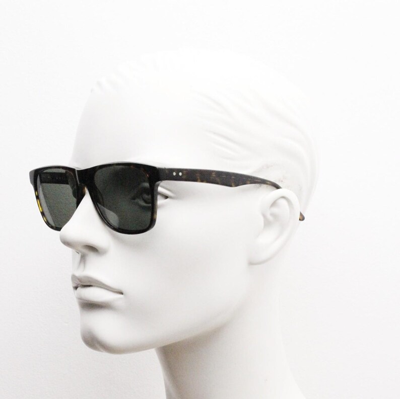 Puede incluir: Un par de gafas de sol de carey con lentes verde oscuro. Las gafas est&aacute;n en una cabeza de maniqu&iacute; blanca.