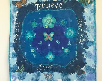 Könnte beinhalten: Ein blaues Wandbehang mit den Worten "Believe, Hope, Faith, Love" in weißer Schrift. Das Kunstwerk zeigt Schmetterlinge und Blumen in Blautönen, mit einem hellblauen Rand und einem Holzstab zum Aufhängen.