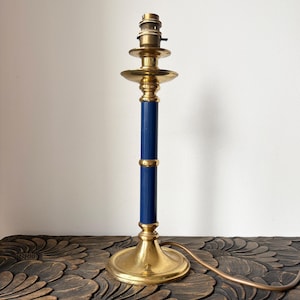 May include: A vintage table lamp with a brass base and accents, featuring a navy blue central column. The lamp has a classic design with a round base and a bulb socket at the top. The lamp is approximately 30 cm tall.