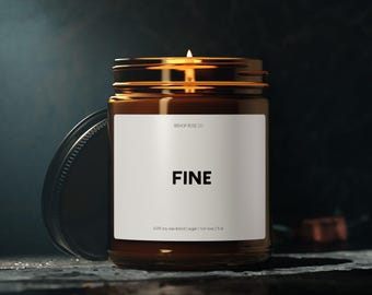 May include: A lit candle in a brown glass jar with a black lid. The label reads "FINE" in bold black letters. The candle is on a dark surface with a dark background.