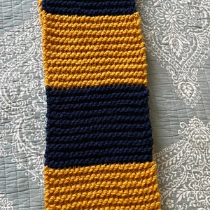 May include: A striped knitted throw blanket in mustard yellow and navy blue. The blanket is made of chunky yarn and has a textured, woven look.