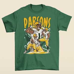 Könnte beinhalten: Grünes T-Shirt mit einer Grafik eines Footballspielers in gelb-weißer Uniform. Das Wort "PARSONS" ist gelb über dem Spieler aufgedruckt. Das Shirt besteht aus einem weichen, bequemen Material.